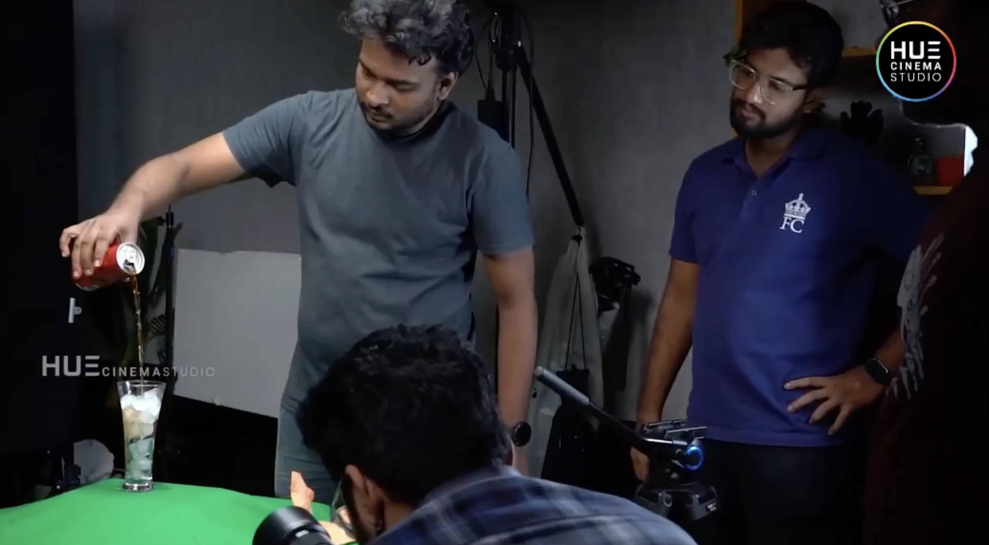Director Haran Reddi pouring Coca-Cola into a glass of ice with crew members beside him during the Alkor Cyber Space b-roll shoot, Hue Cinema Studio.